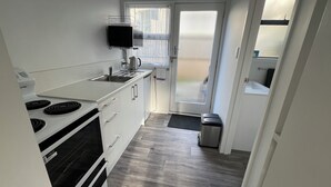 A compact kitchen with white cabinets, a stove, and a sink. - Diplomat Motel (Christchurch)