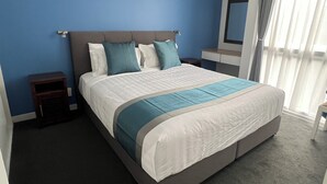 A modern hotel room with a large bed, a nightstand, a dresser, and a mirror. - Diplomat Motel (Christchurch)
