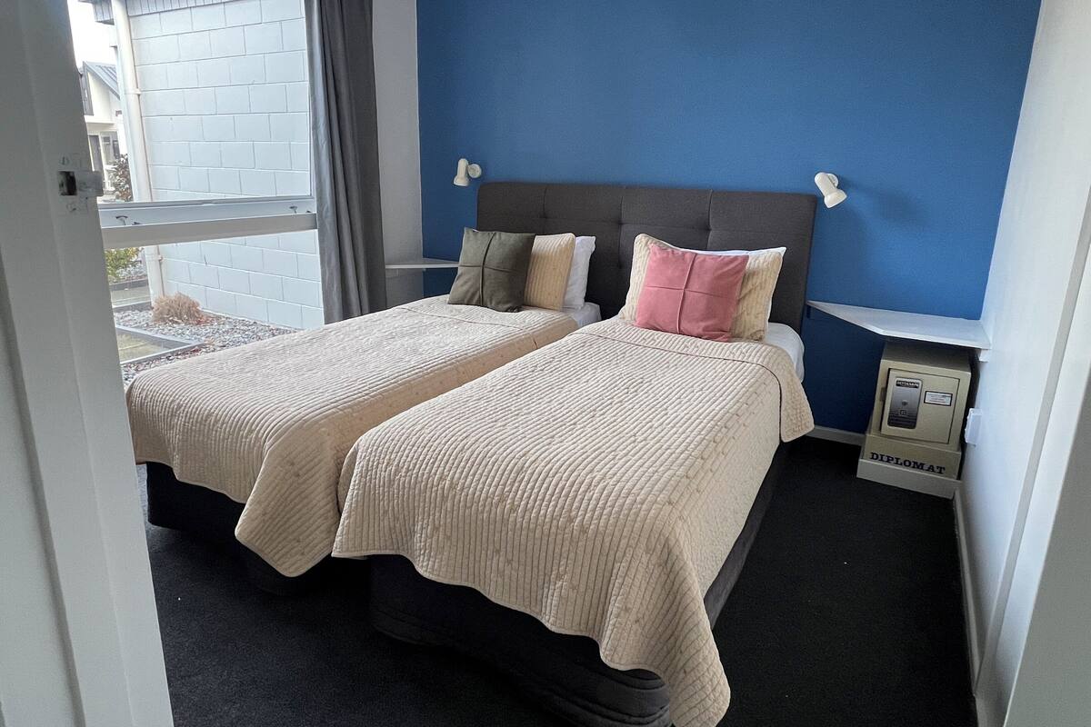 A double bed with two pillows, a nightstand, a lamp, and a small safe.