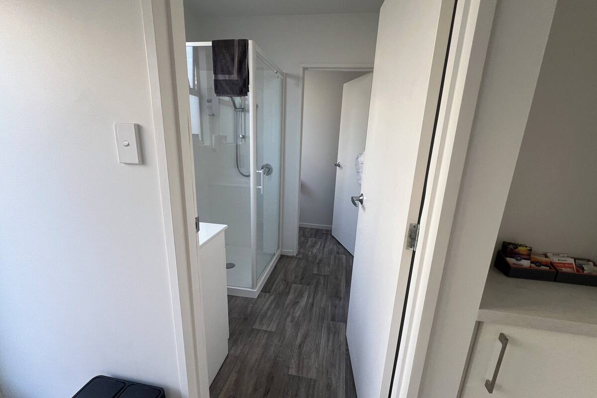 A narrow hallway leading to a bathroom with a glass shower enclosure and a white sink.