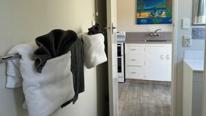 A hotel room with a bathroom and kitchenette. There are towels hanging on the wall, a painting on the wall, and a sink in the kitchenette. - Diplomat Motel (Christchurch)