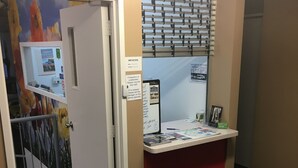 Un espace d’accueil comprenant un comptoir, un téléphone fixé au mur et une porte donnant sur un escalier.