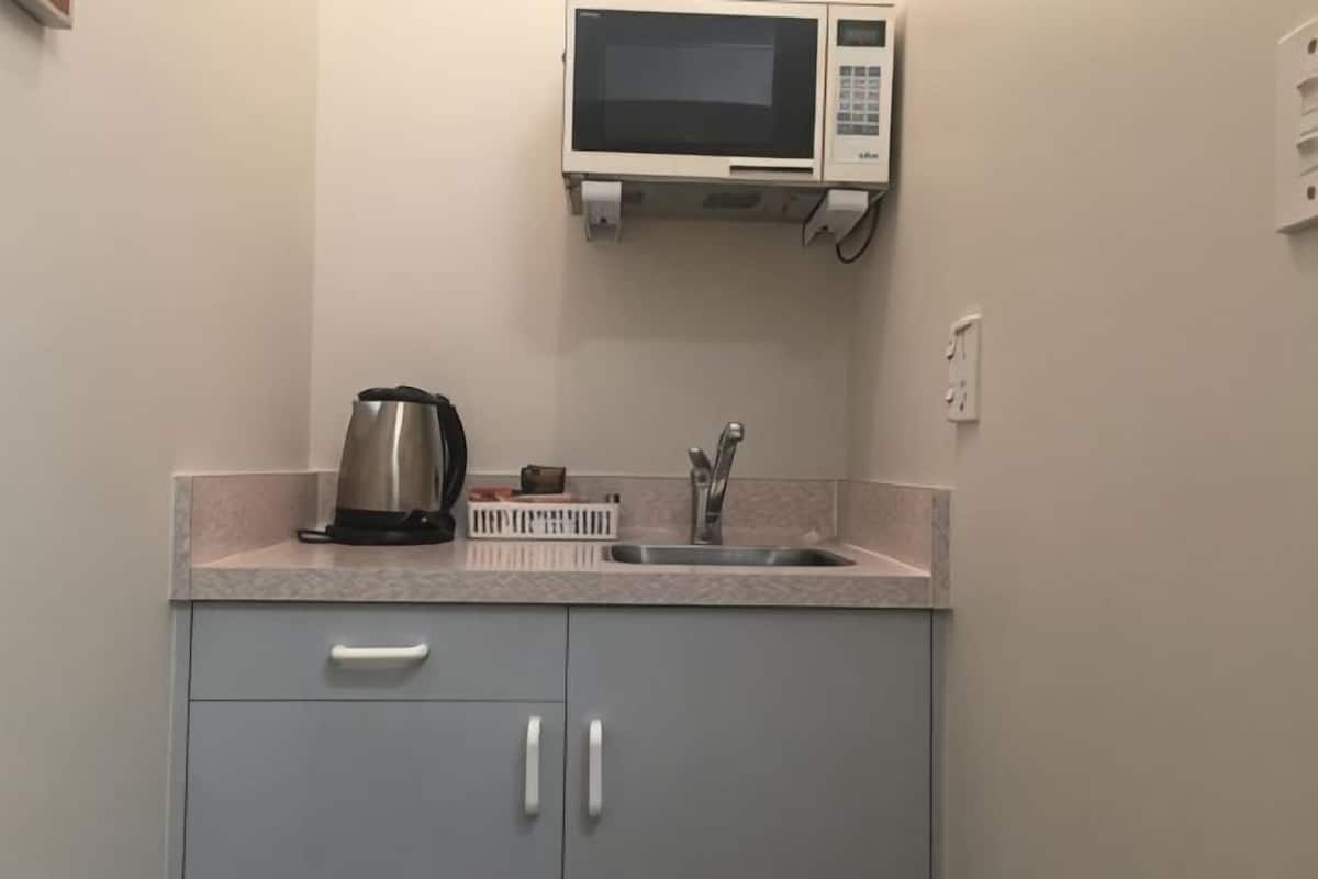 A kitchen with a microwave, kettle, and sink.