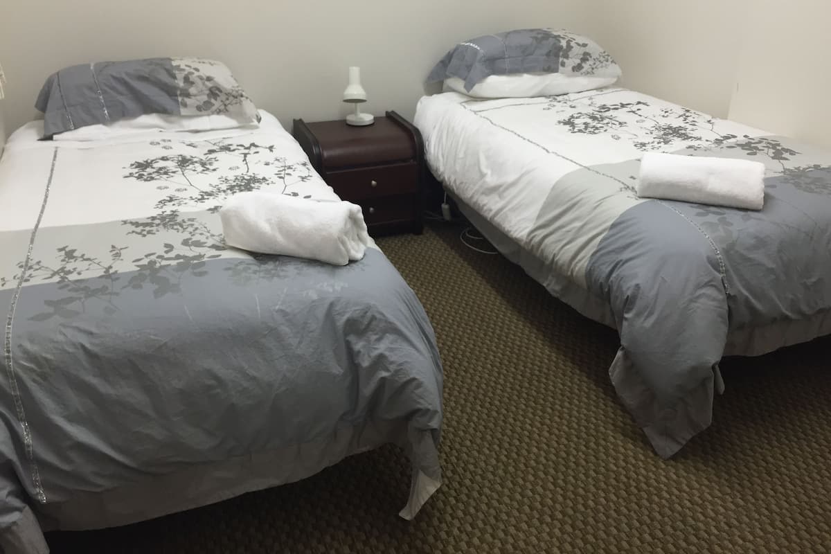 A hotel room with two single beds, each with a floral-patterned duvet and pillow, a bedside table with a lamp, and a carpeted floor.