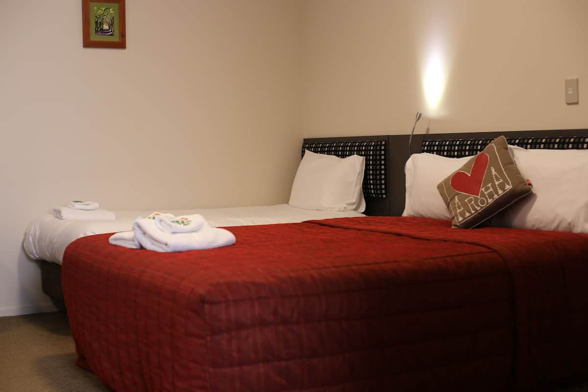 A hotel room with two beds, a red blanket on the left bed, white linens on the right bed, and a pillow with a heart design.