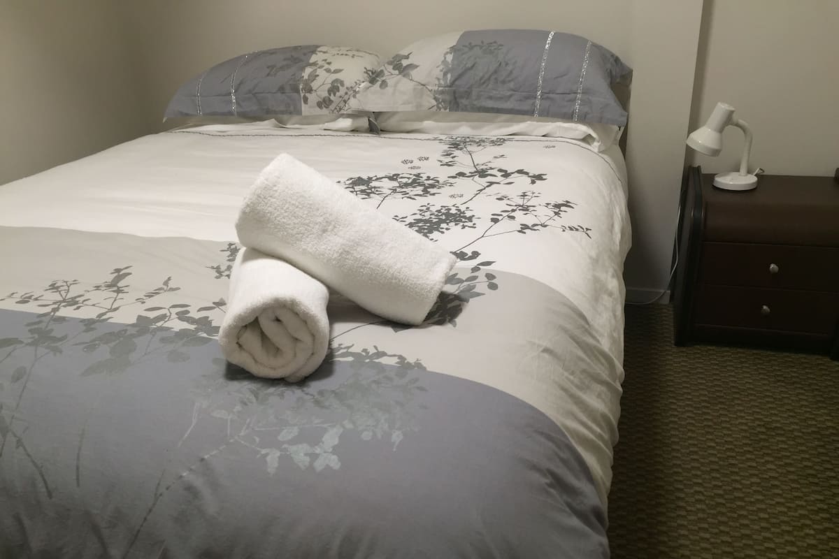 A neatly made bed with a rolled white towel, a floral-patterned bedspread, and a bedside table with a lamp.