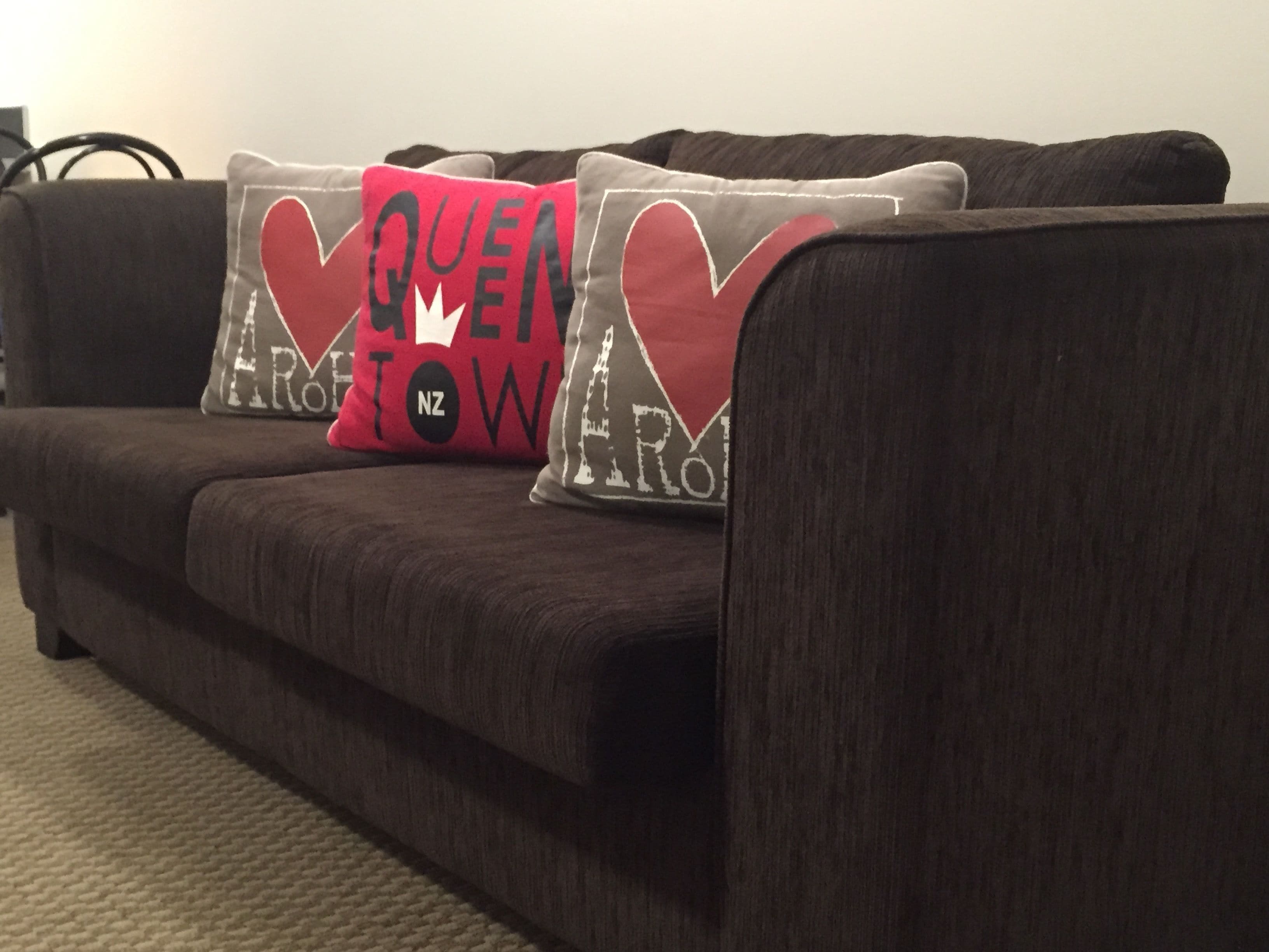 A dark brown sofa with two decorative pillows featuring a red and white design.