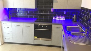 Une cuisine moderne avec des meubles gris, un dosseret en carreaux noirs et un éclairage bleu sous les meubles.
