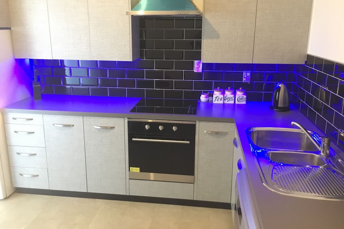 A modern kitchen with grey cabinets, a black tiled backsplash, and blue under-cabinet lighting.