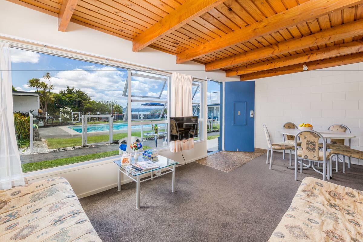 A room with a large window, a glass table, a sofa, a dining table with chairs, and a blue door.
