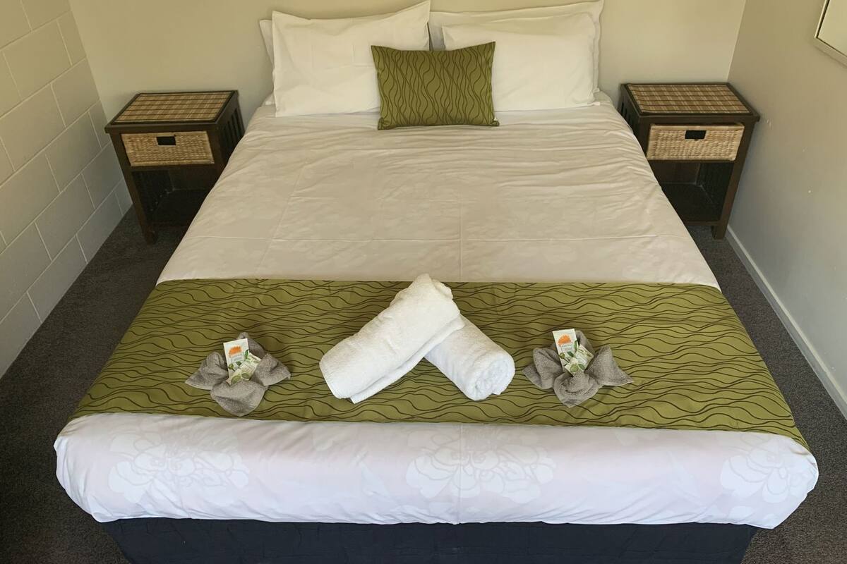 A neatly made bed with white linens, a green patterned bedspread, and two nightstands with wicker baskets.