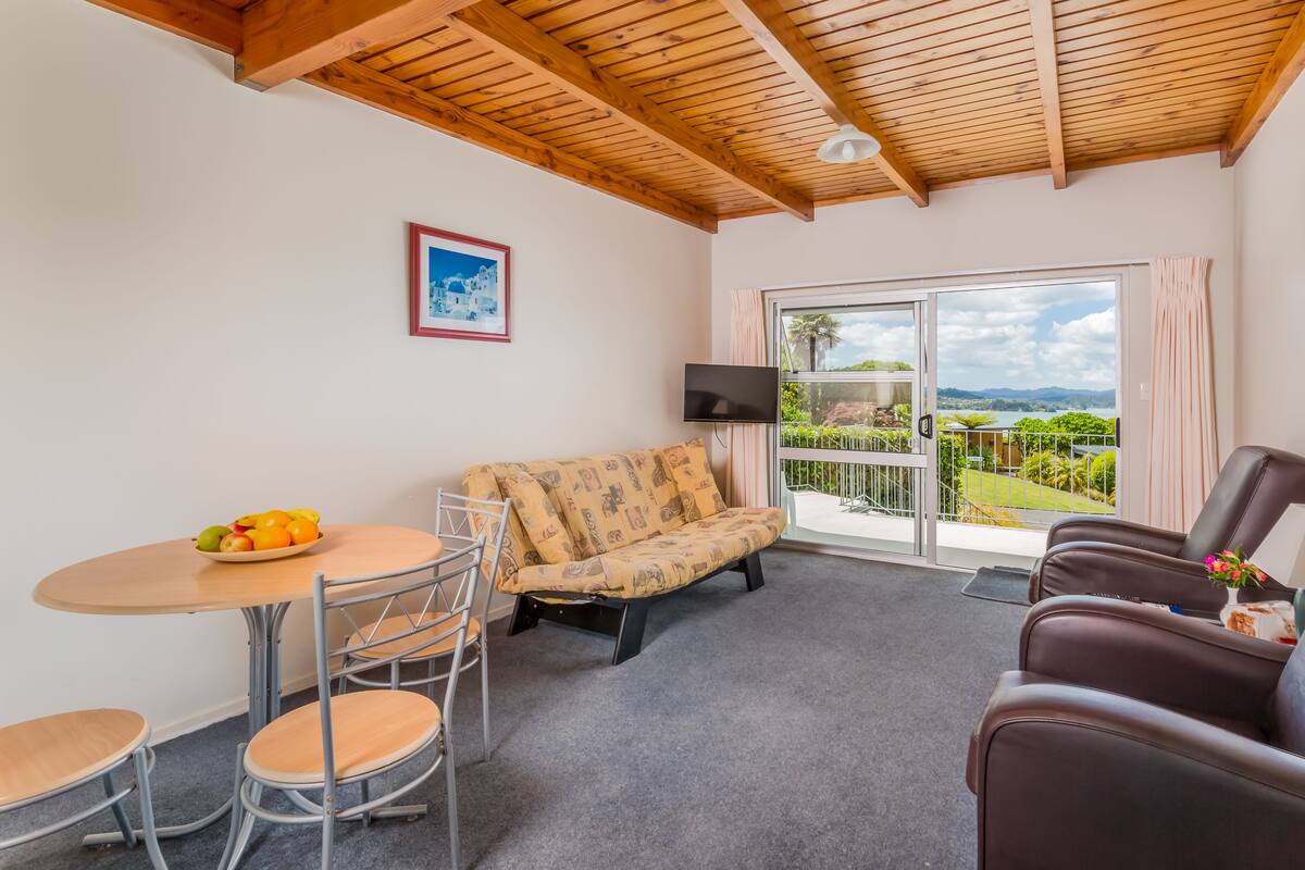 A cozy room with a wooden ceiling, a sofa, a table with fruit, and a TV.