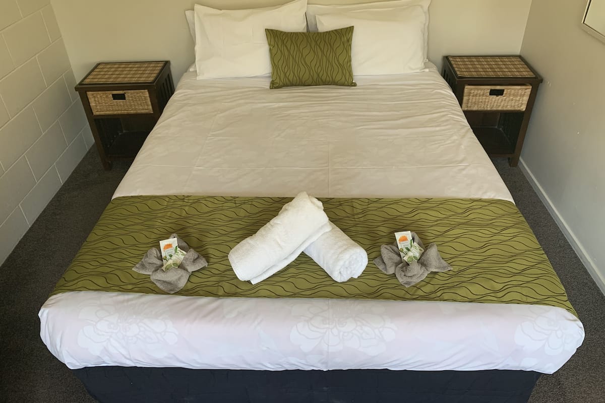 A neatly made bed with white linens, a green patterned bedspread, and two nightstands with wicker baskets.