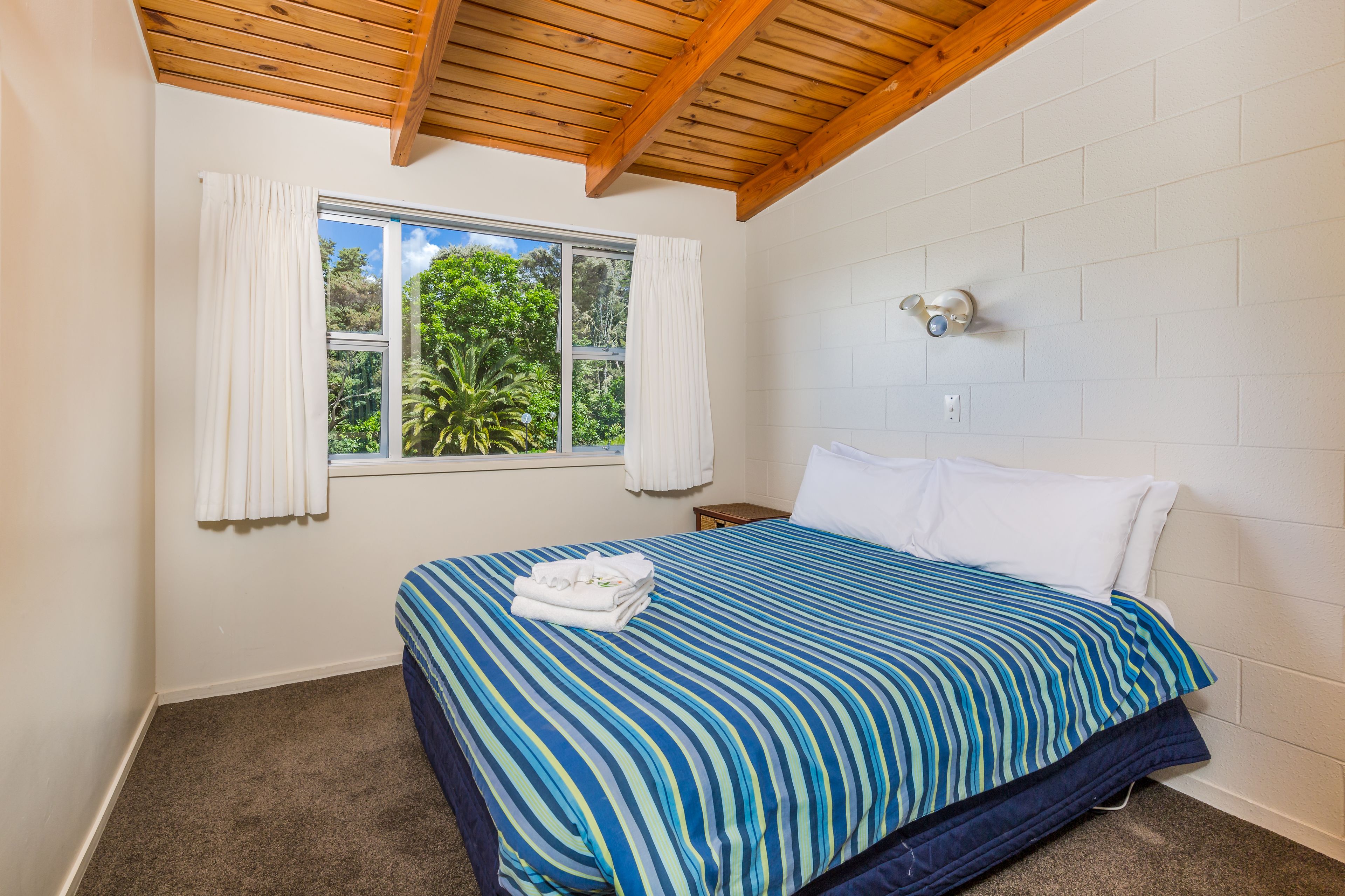 Um quarto com cama, janela com cortinas, mesa de cabeceira e luminária na parede.