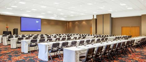 A large conference room with rows of tables and chairs, a projector screen, and a carpeted floor.