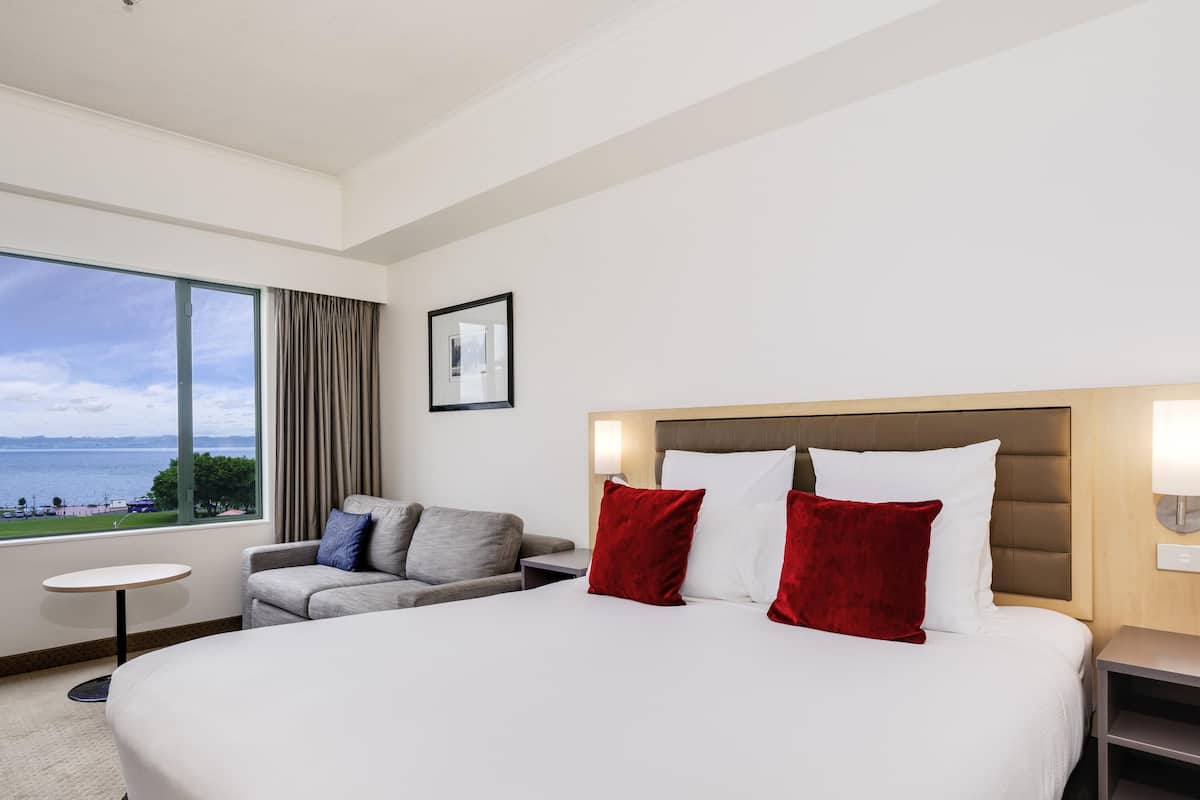 A hotel room with a large bed, a sofa, a small table, and a view of the sea.
