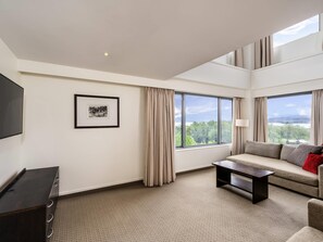 A modern living room with a sofa, a coffee table, a TV, and a large window with curtains.