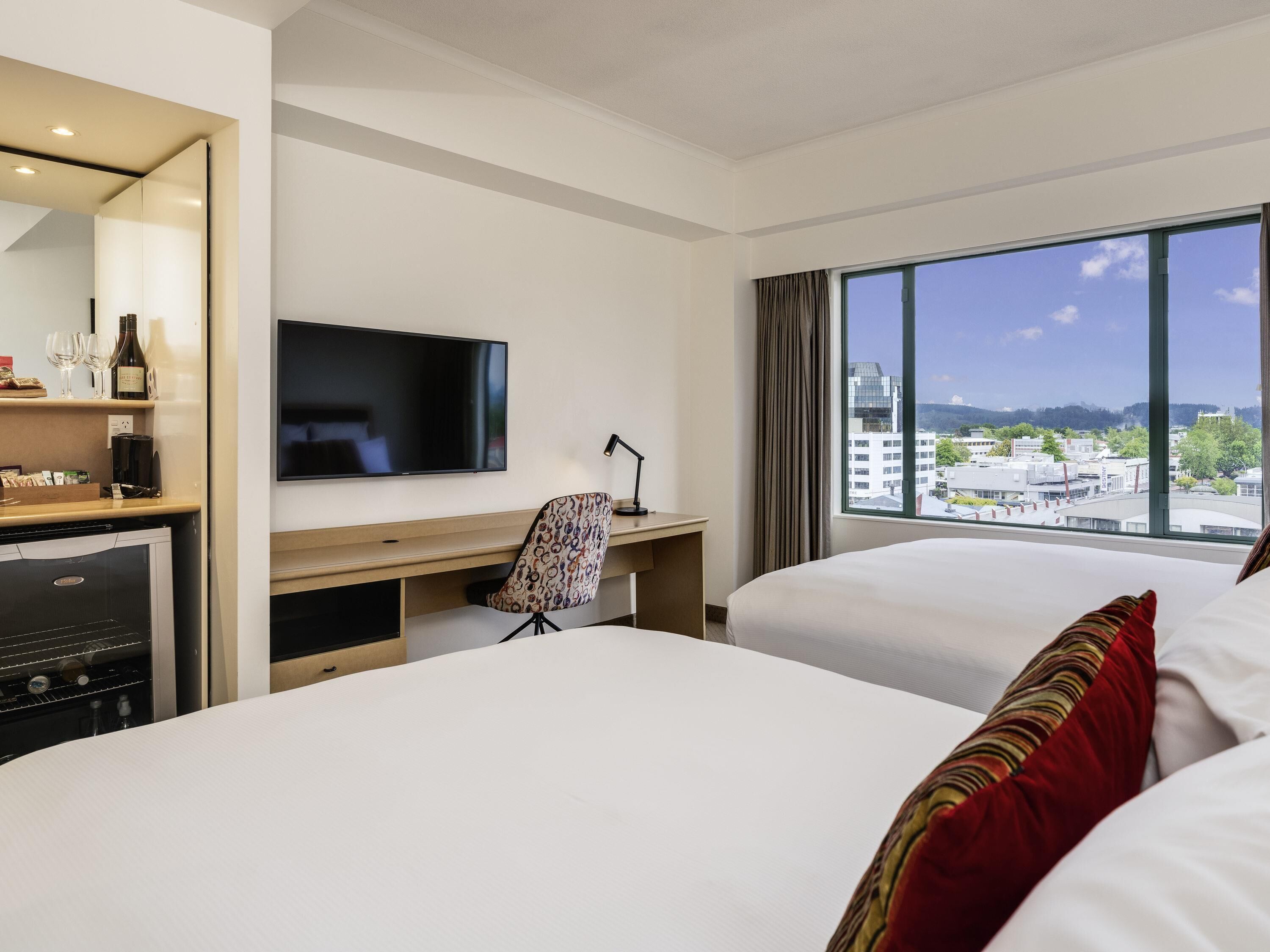 Habitación de hotel con dos camas, un escritorio, un televisor y vistas a la ciudad.