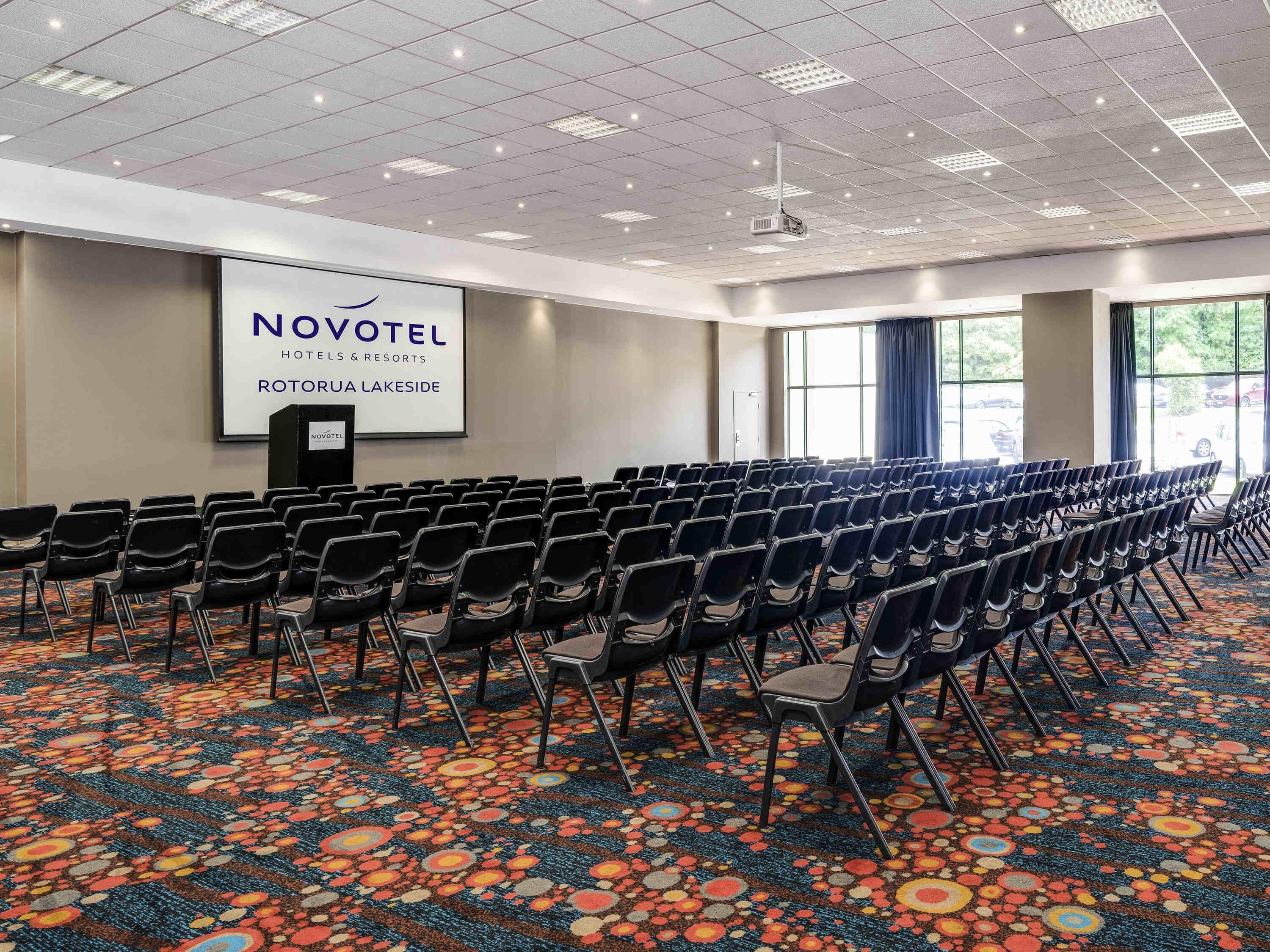 A conference room with rows of chairs, a projector screen, and a carpeted floor.