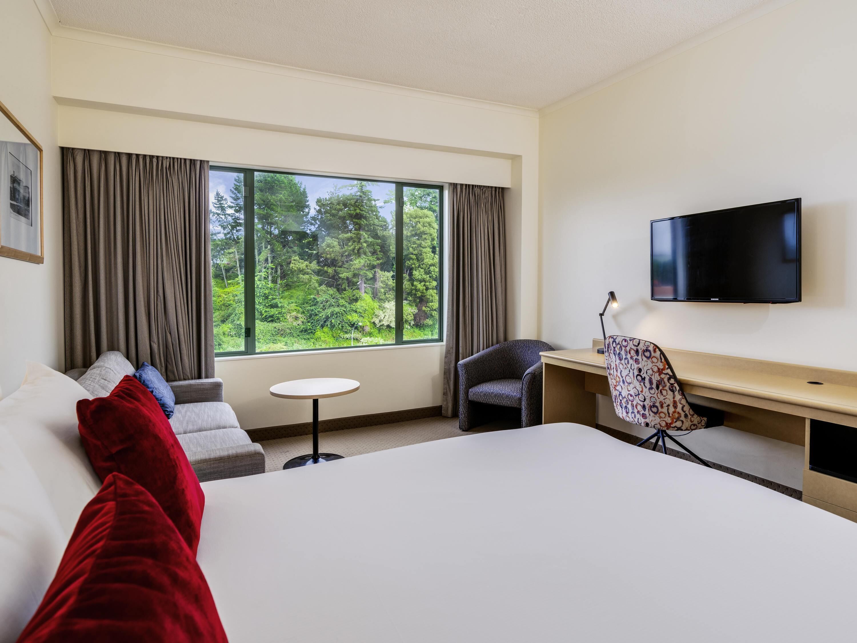 Habitación de hotel con cama, escritorio, silla, televisor y ventana con cortinas.