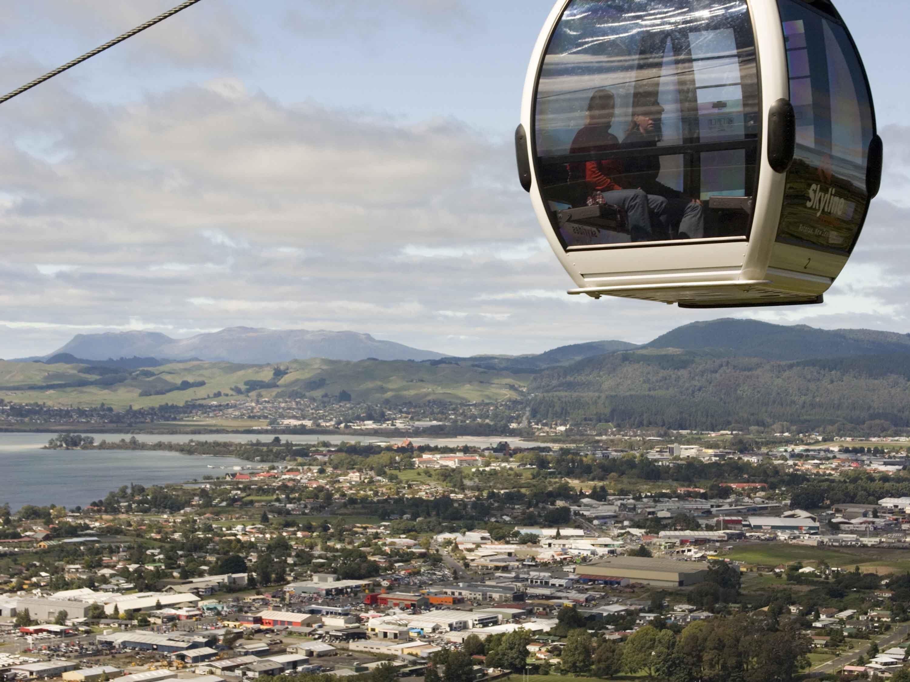 A cable car with passengers, a town below, and mountains in the background.