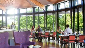 A restaurant with large windows, wooden ceiling beams, and purple chairs.