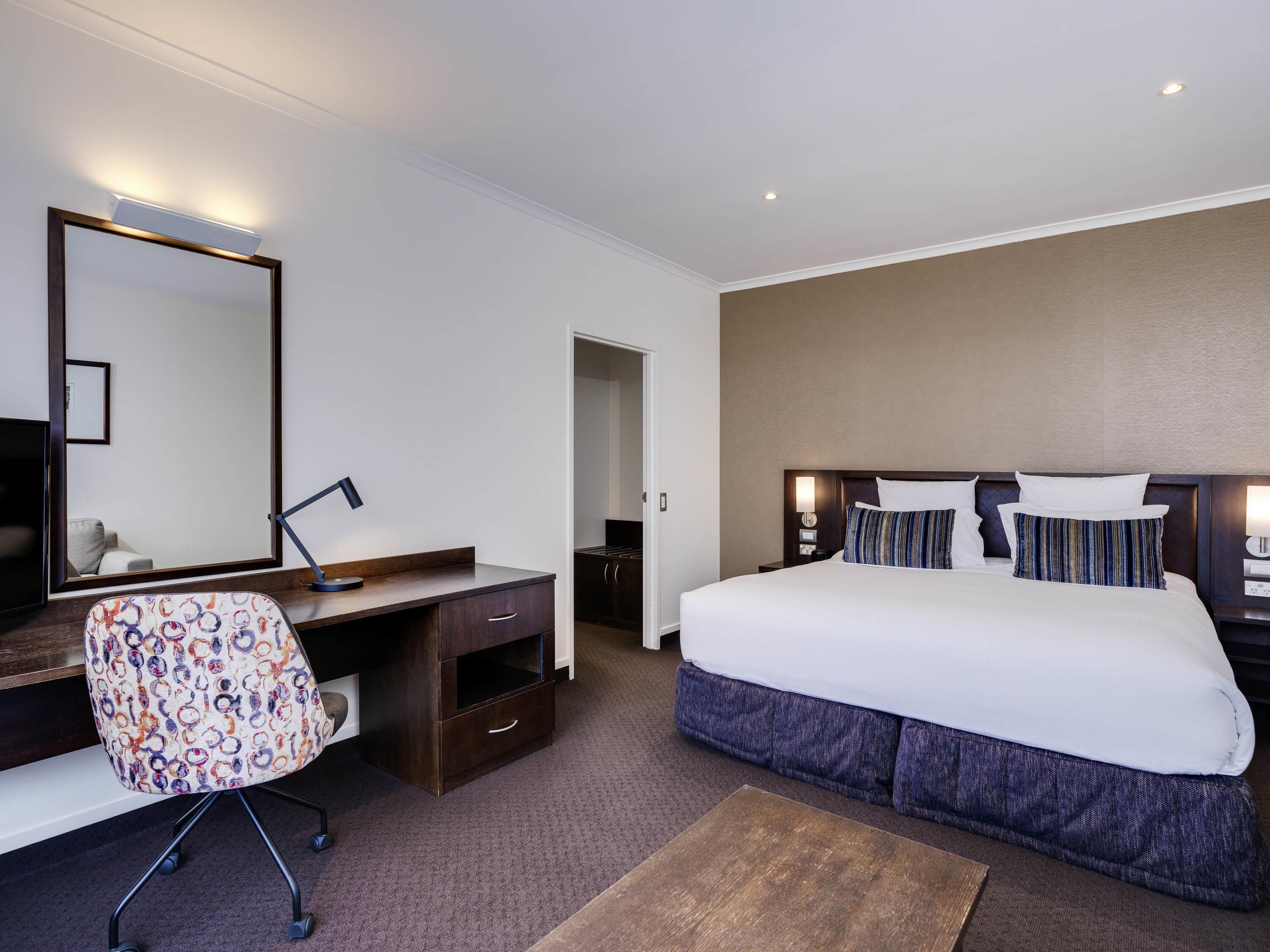 A hotel room with a bed, desk, chair, and a large mirror.