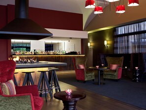A bar area with a fireplace, seating with red and green upholstery, and a bar stocked with bottles.