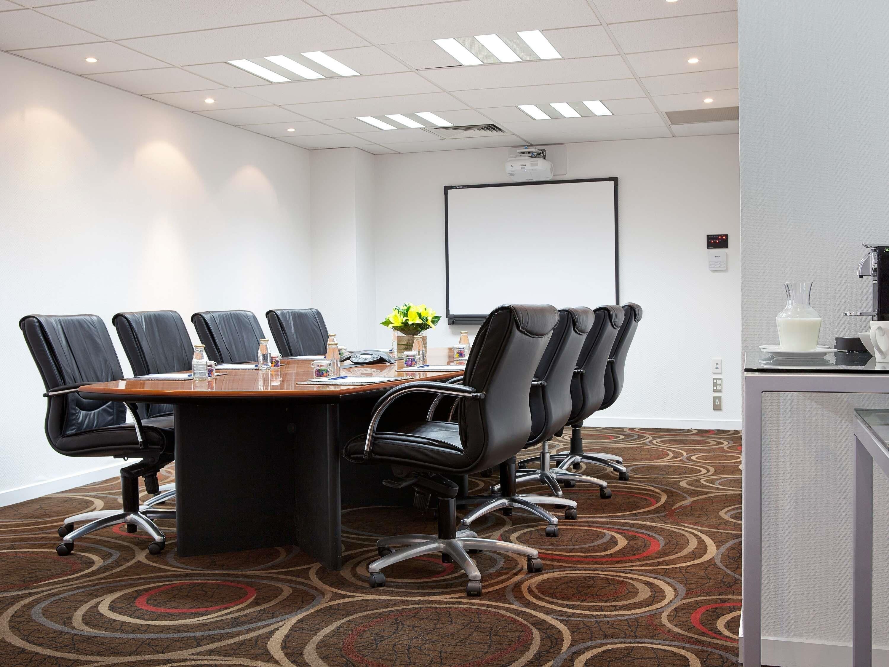 A conference room with a long table, black chairs, a projector screen, and a coffee station.