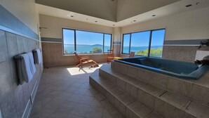 A spa area with a hot tub, seating, and large windows overlooking a scenic view. - Novotel Rotorua Lakeside (Rotorua)