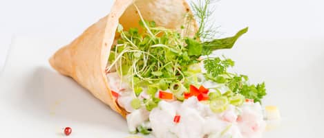 Une galette garnie de divers ingrédients frais, comme des légumes verts, des poivrons rouges et, éventuellement, un type de viande ou de fruits de mer, posée sur une surface blanche.