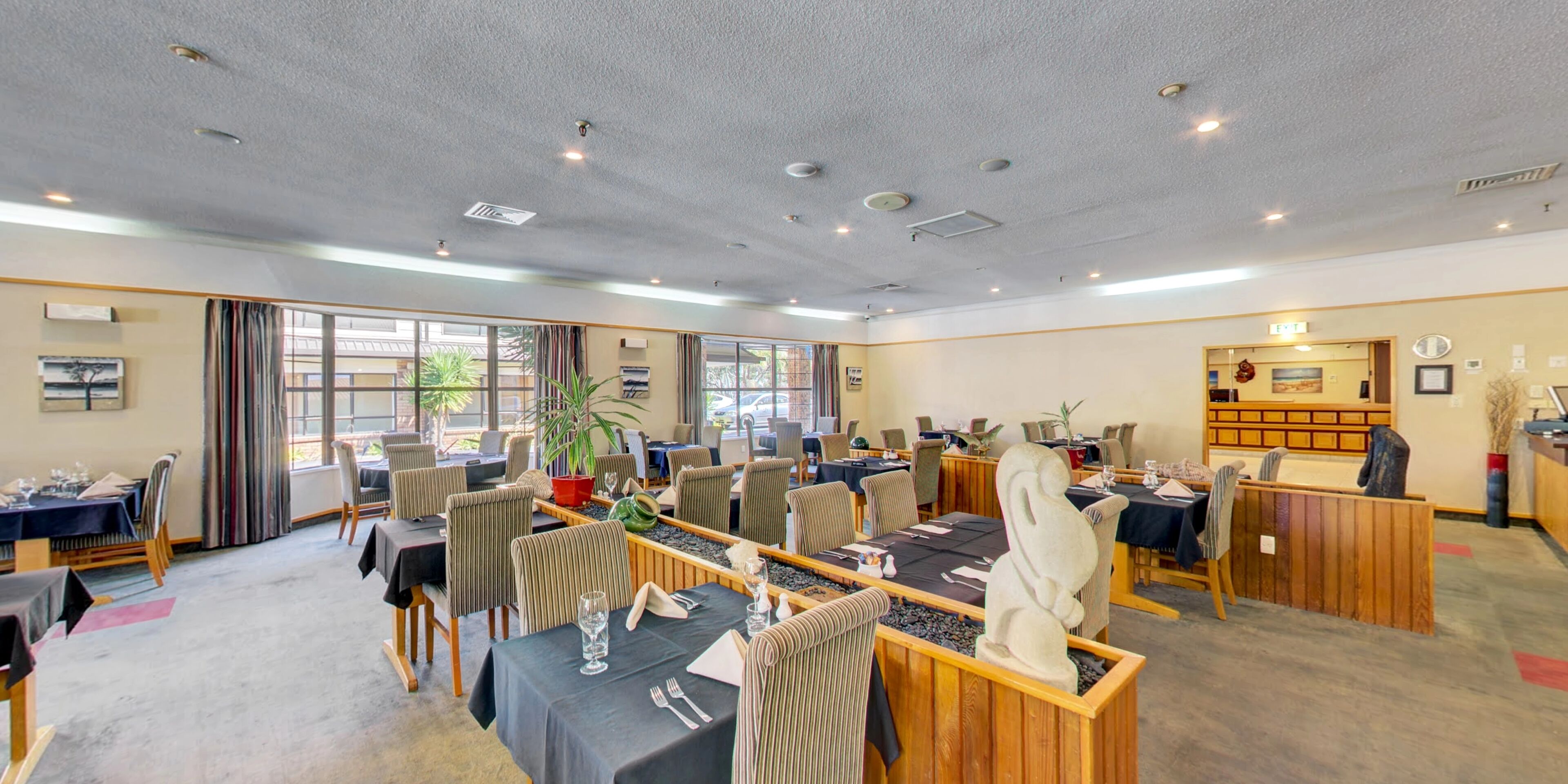 A hotel dining area with multiple tables, chairs, and a reception desk.