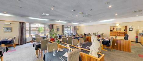 A hotel dining area with multiple tables, chairs, and a reception desk.