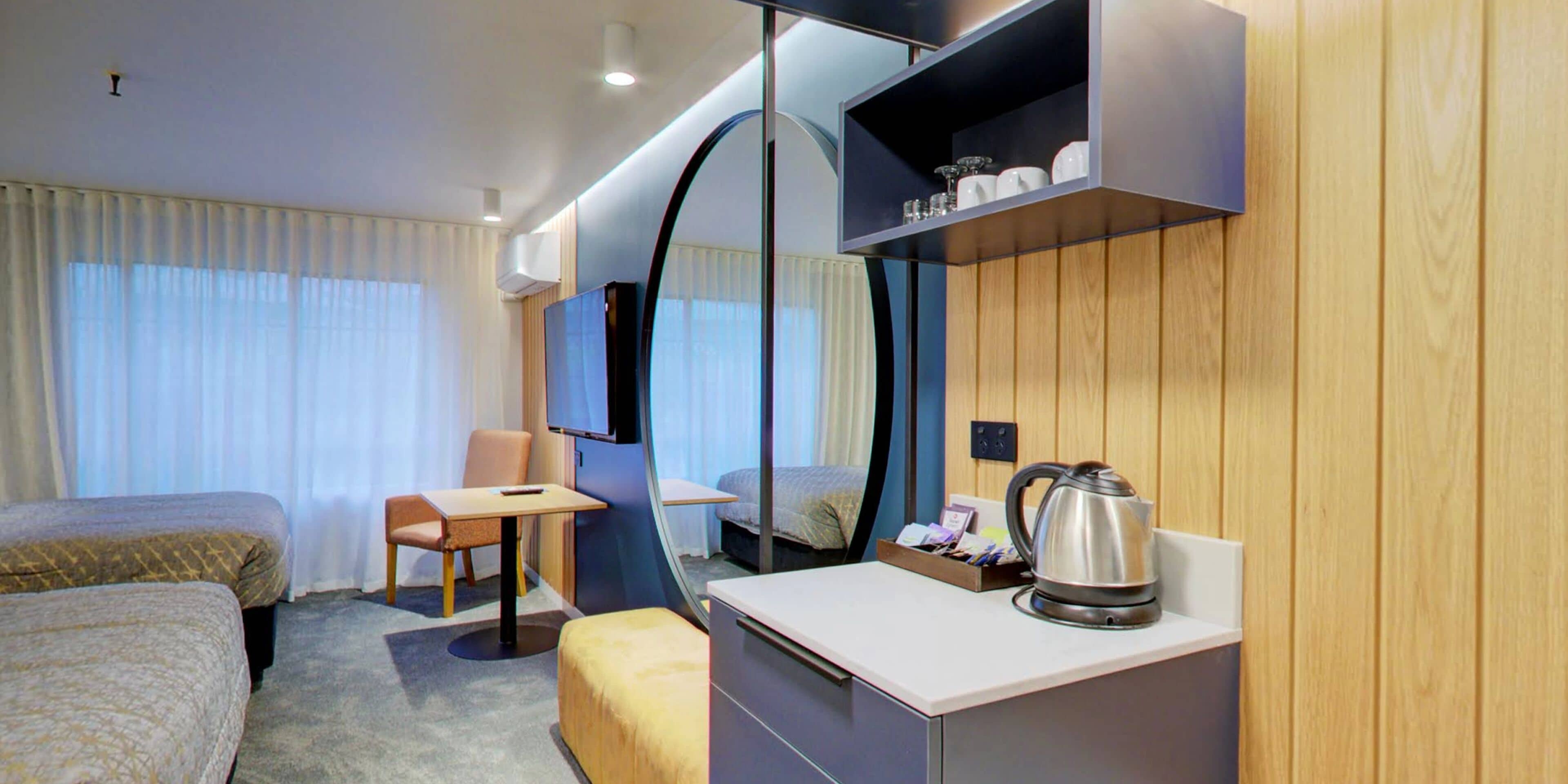 A hotel room with two beds, a desk, a chair, a television, and a coffee maker.