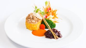 Un plato blanco con un bocado de comida cubierto de pan rallado, una zanahoria pequeña, una cucharada de salsa y una guarnición de verduras.
