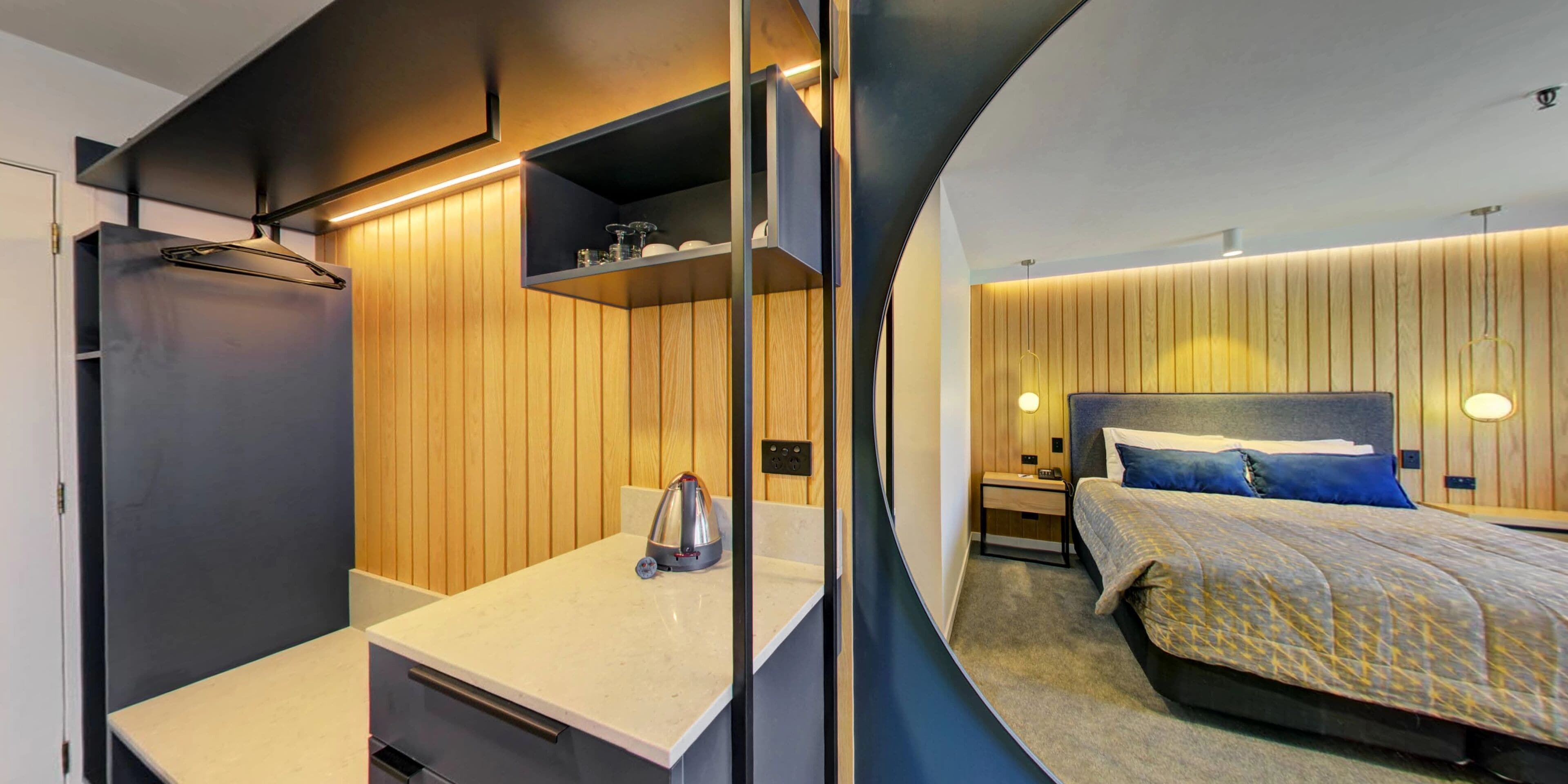 Ein modernes Hotelzimmer mit einer Wandpaneele aus Holz, einem Bett mit einem gemusterten Überwurf, einem Nachttisch und einem integrierten Kleiderschrank.