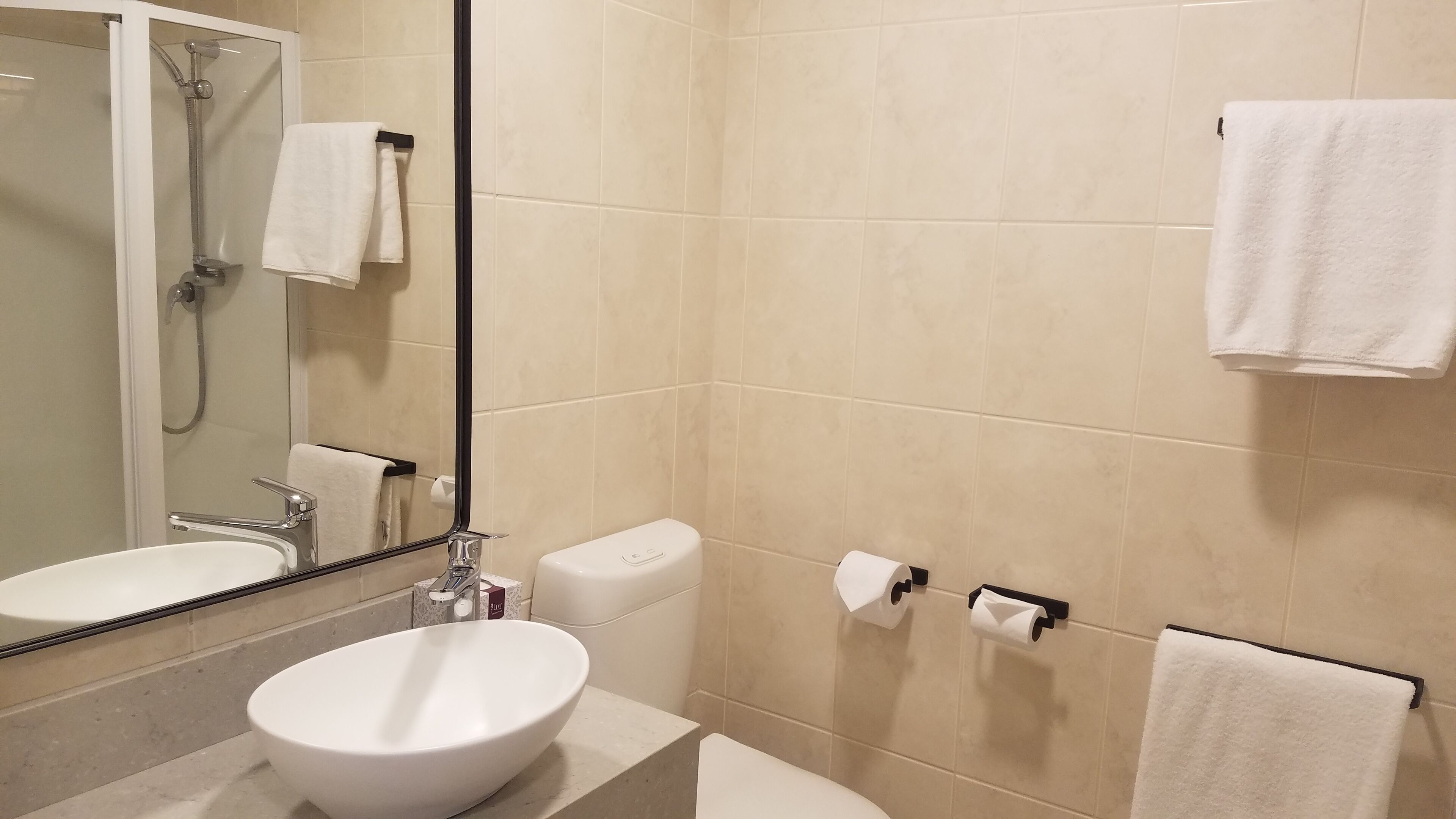 A modern bathroom with a white sink, mirror, and shower. There are two white towels hanging on hooks.