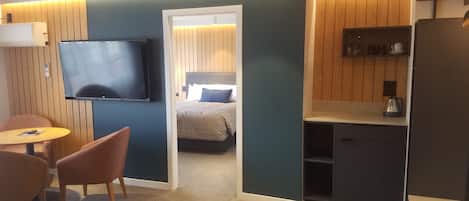 Una habitación de hotel con televisión, cama, kitchenette pequeña y zona de estar con mesa y sillas.
