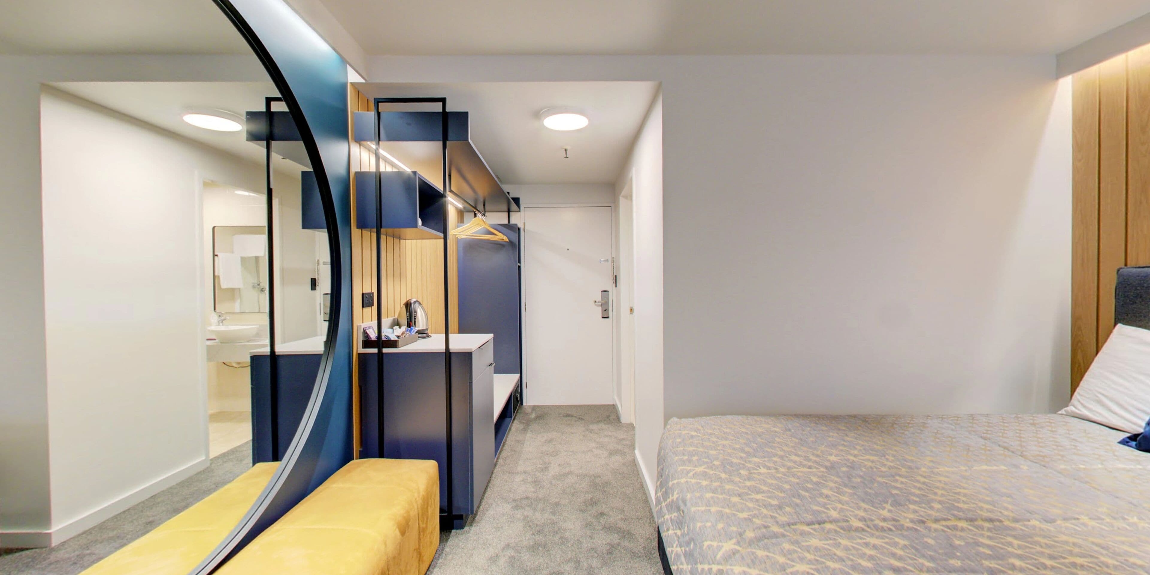 Une chambre d’hôtel moderne équipée d’un lit, d’une banquette, d’un bureau et d’un miroir.
