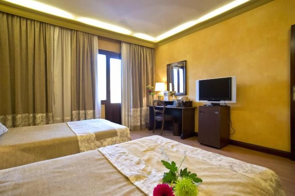 A hotel room with two beds, a desk, a television, and a window with curtains.
