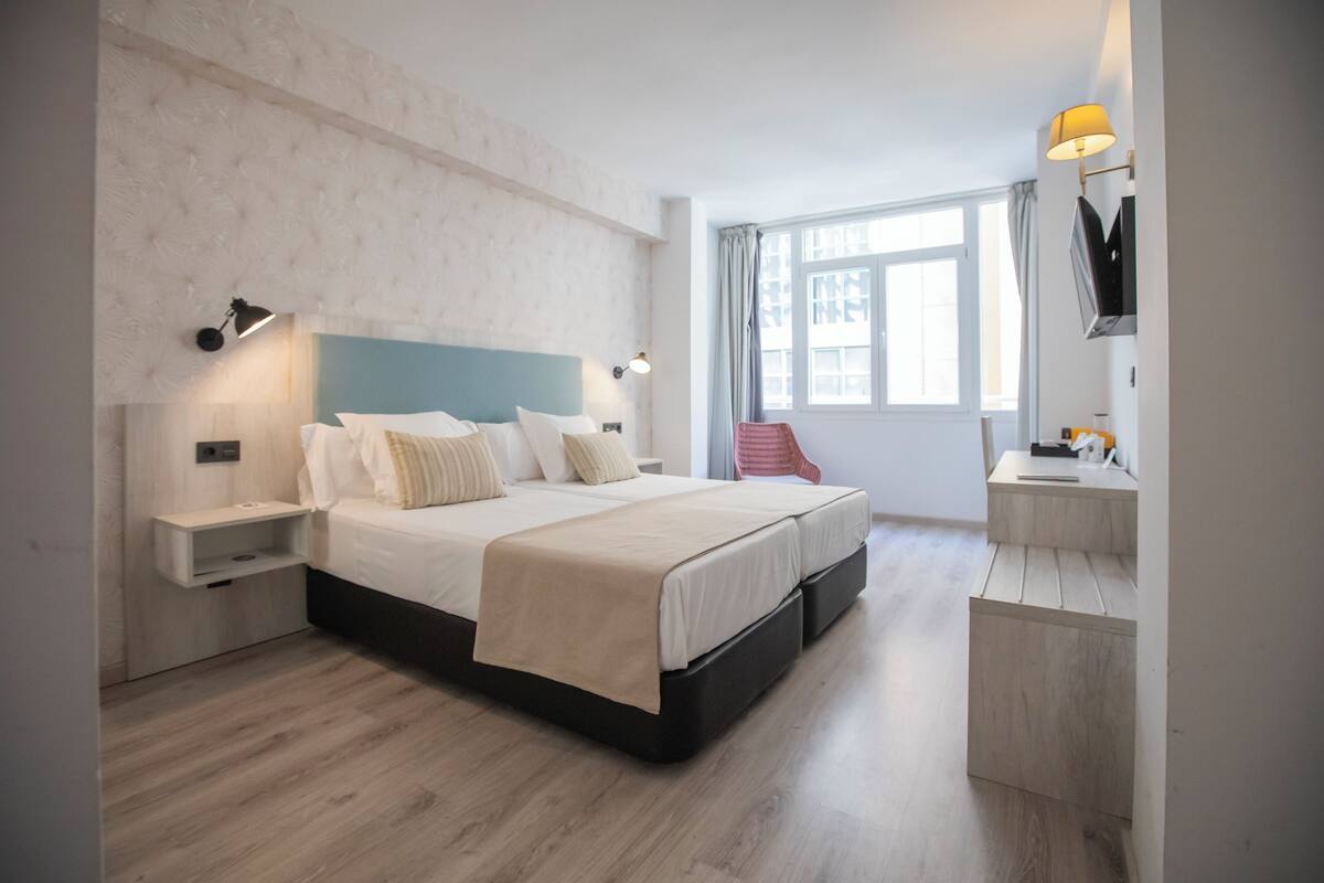 Quarto de hotel moderno com uma cama grande, mesas de cabeceira, escrivaninha e uma cadeira.