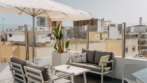 Terraza en la azotea con una sombrilla blanca, un sofá, una mesa y una planta en maceta.