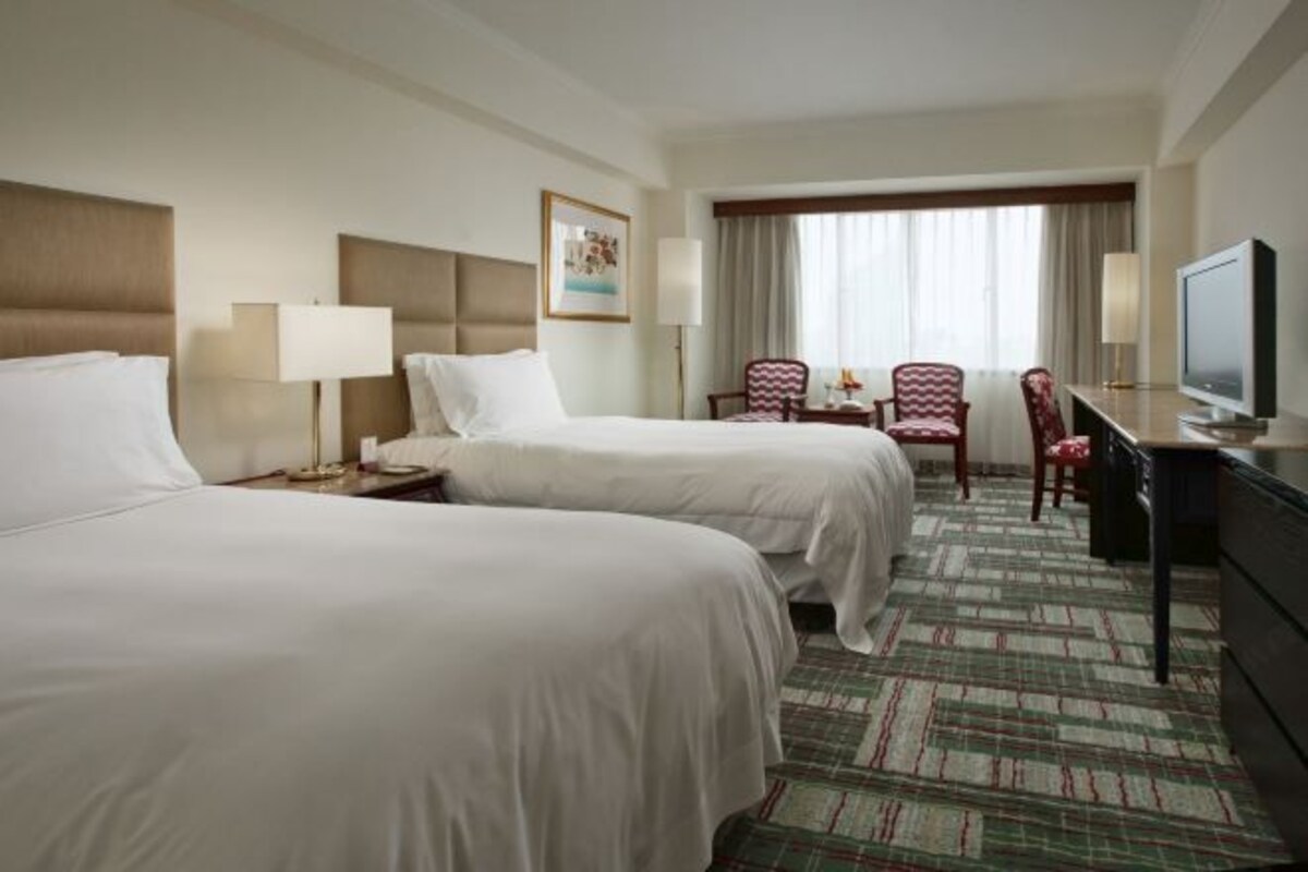 A hotel room with two beds, a desk, a television, and a window with curtains.