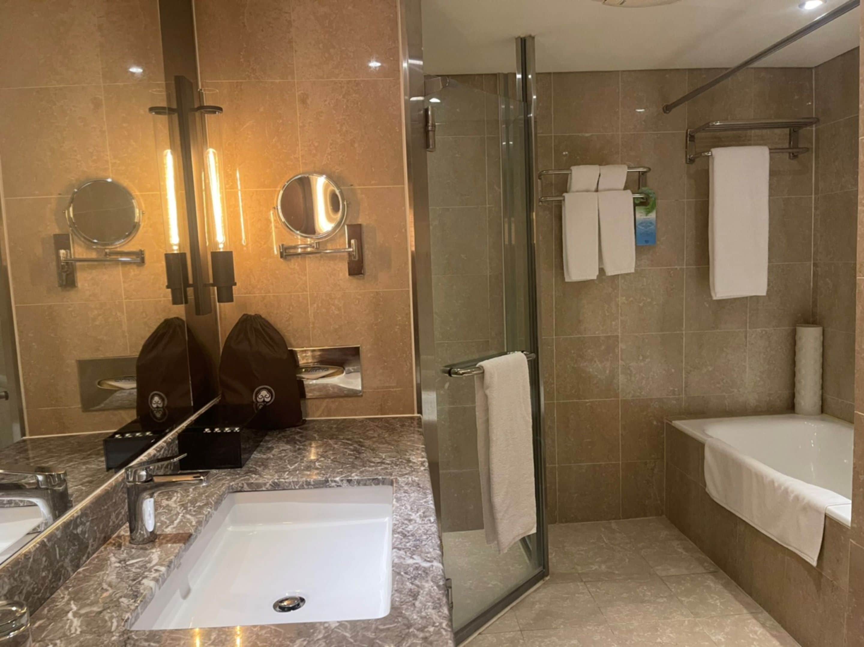 Un baño moderno con un lavabo de mármol, una cabina de ducha de vidrio y dos espejos.