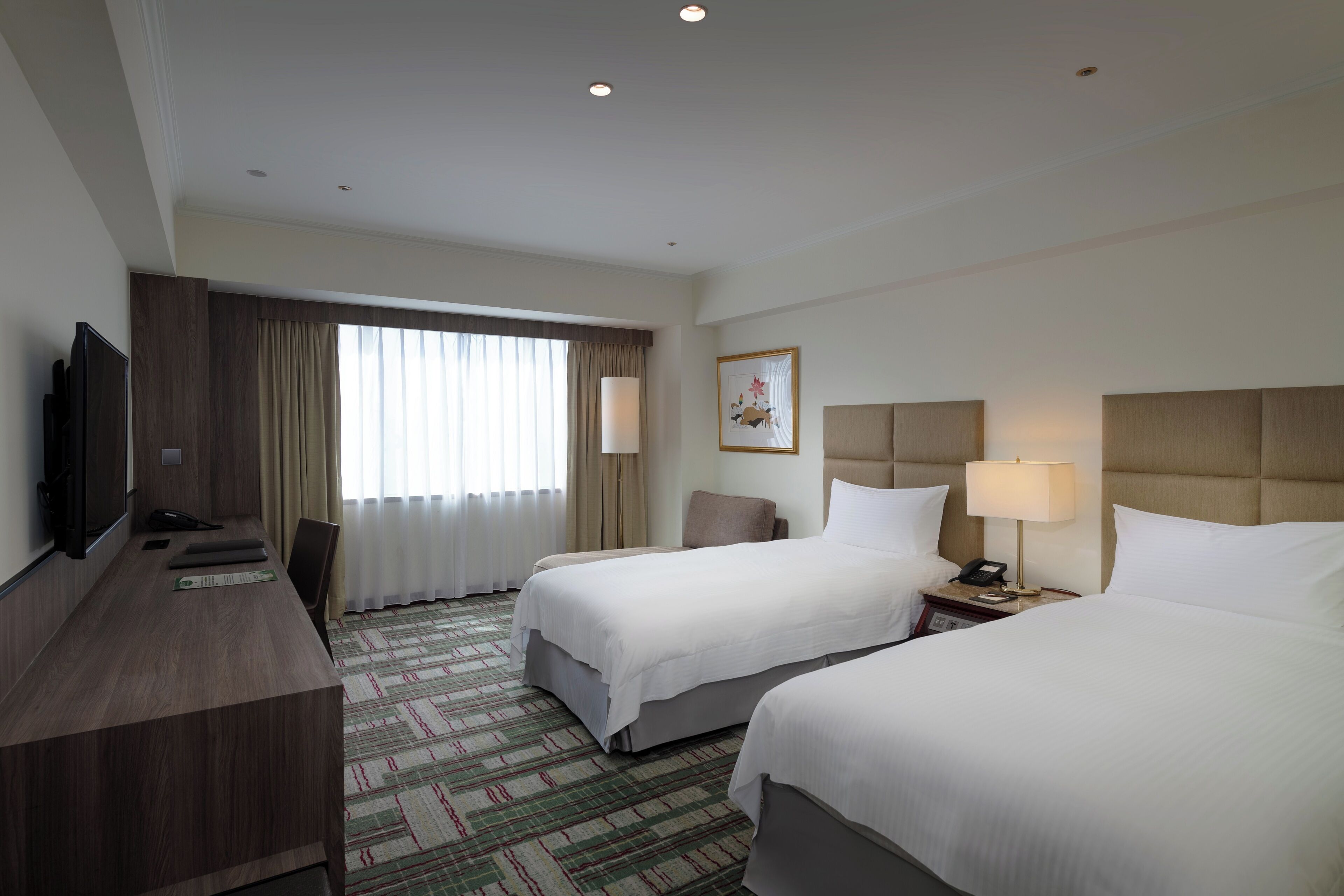 A hotel room with two beds, a desk with a flat-screen TV, a lamp, and a painting on the wall.