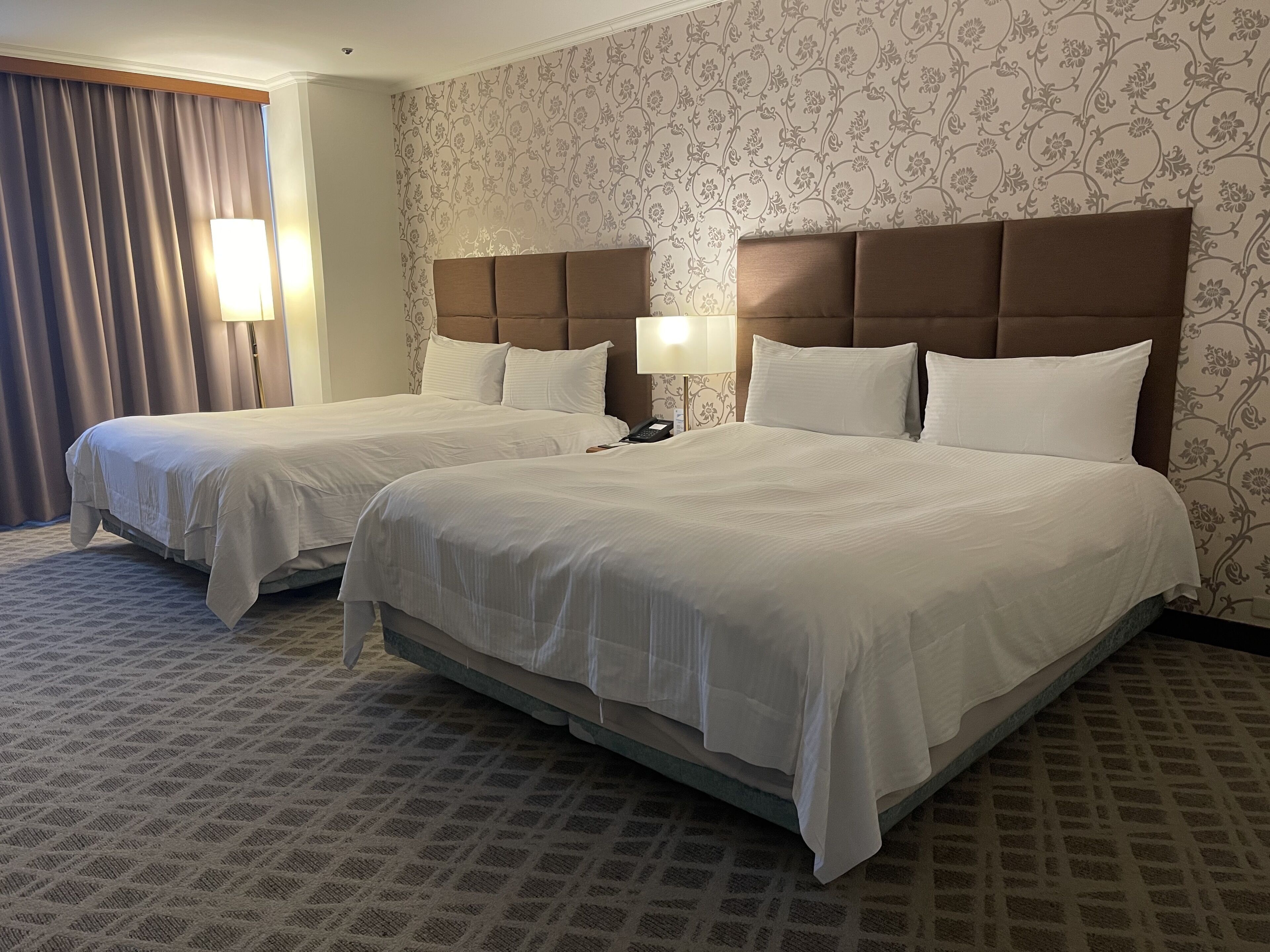 A hotel room with two beds, a patterned wallpaper, and a carpeted floor.