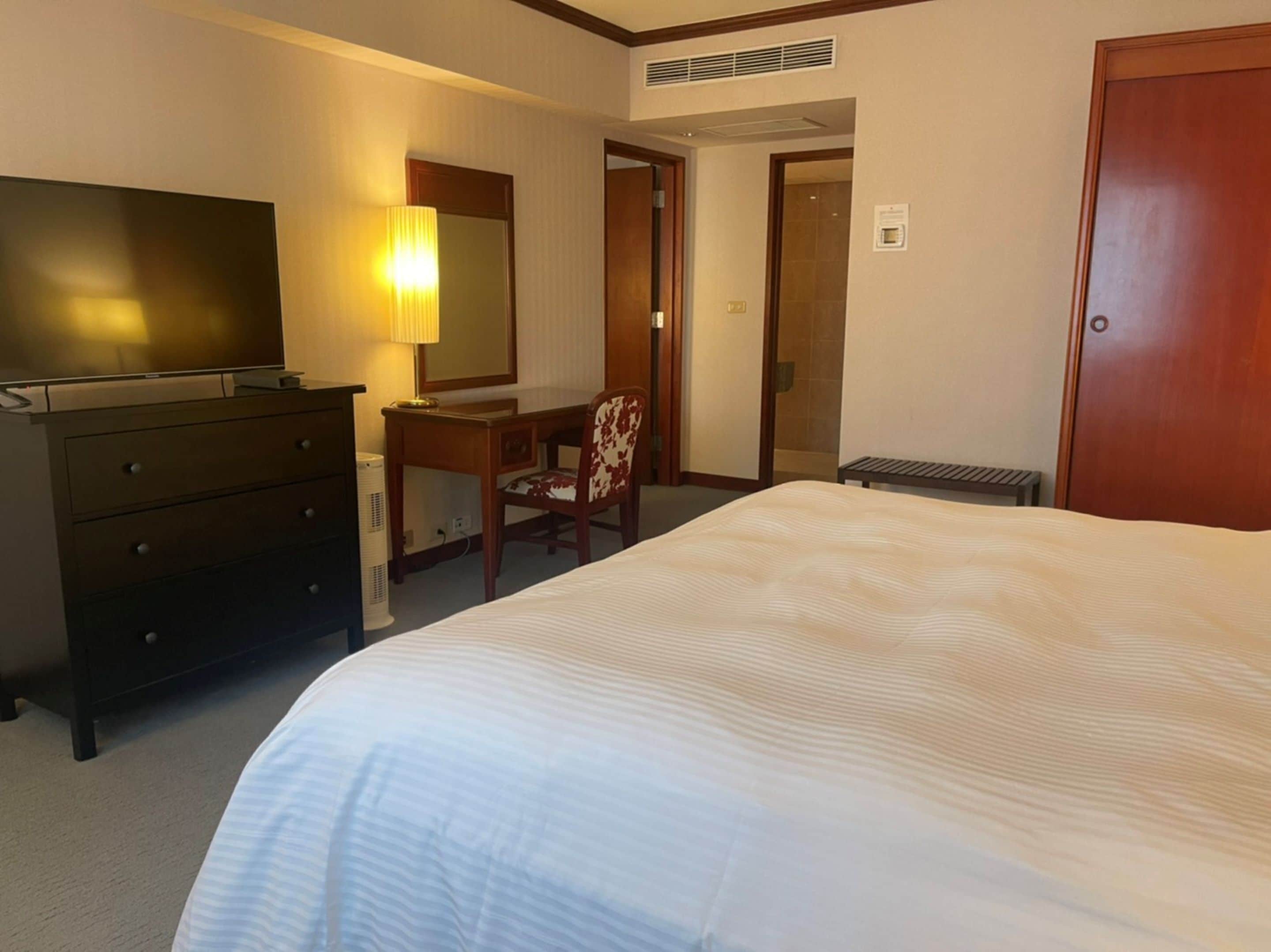 A hotel room with a large bed, a desk with a chair, a television, and a mirror.