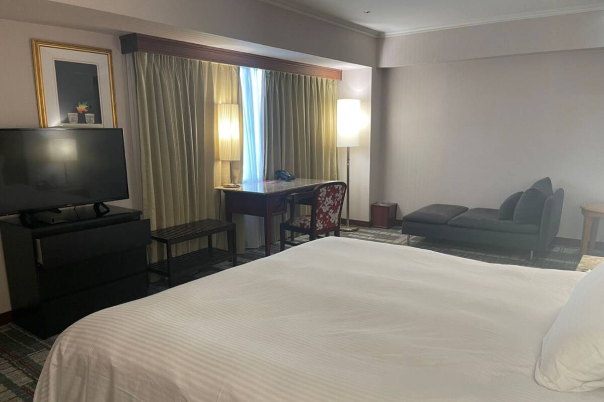 A hotel room with a large bed, a desk with a chair, a television, and a sofa.