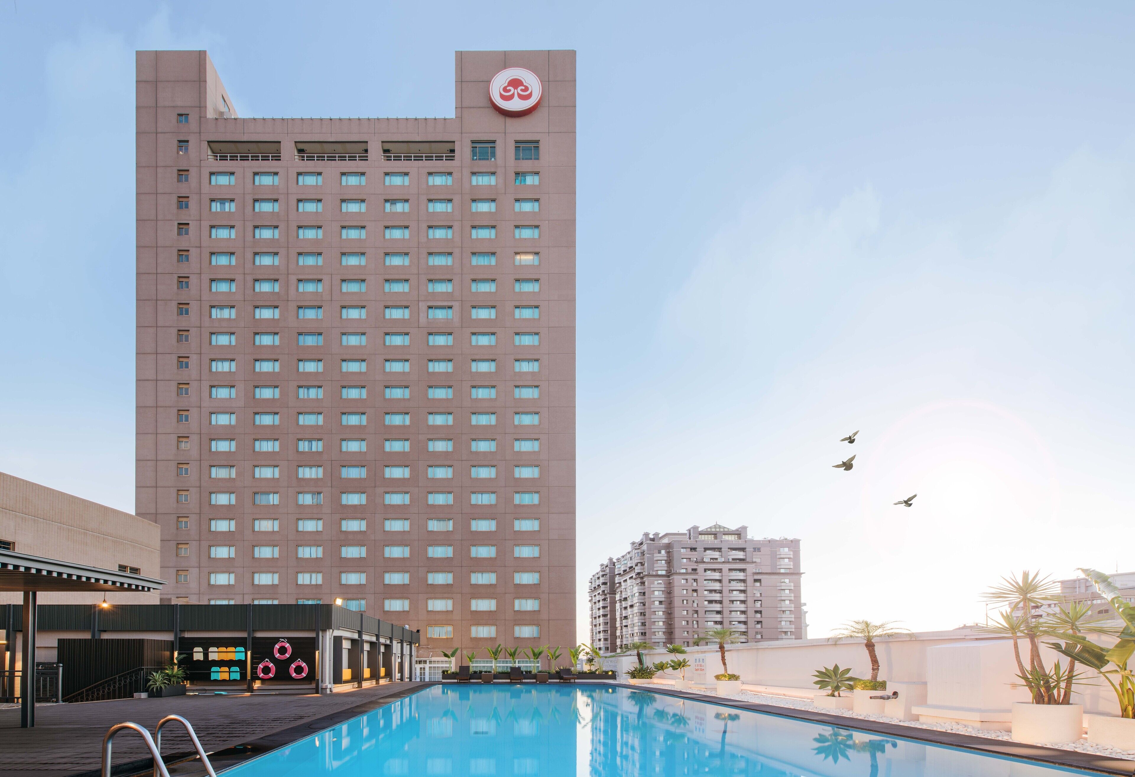A high-rise hotel with a swimming pool, multiple floors, and a clear sky.