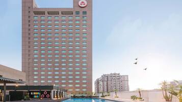 A high-rise hotel with a swimming pool, multiple floors, and a clear sky.